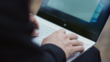 Takım elbiseli bir adam ormanda otururken bir mesajı çabucak bilgisayara basıyor. Yakın plan.