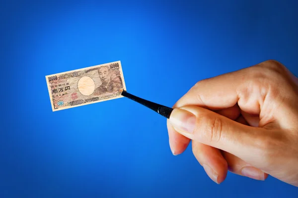 Hand with a pincet holding small banknote — Stock Photo, Image