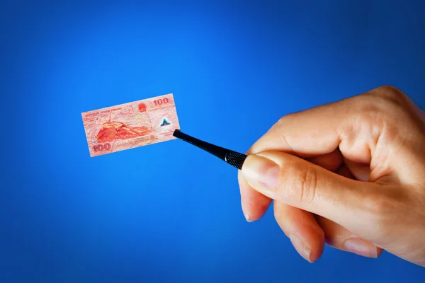 Mano con una pinza que sostiene un billete pequeño —  Fotos de Stock