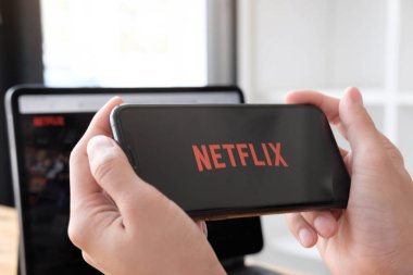CHIANG MAI, THAILAND, MAR 11, 2021: bir hamağın içindeki genç kadın akıllı telefonuyla Netflix 'i açıyor. Milenyum kızı elinde cep telefonu ve ekranında Netflix logosuyla dinleniyor.