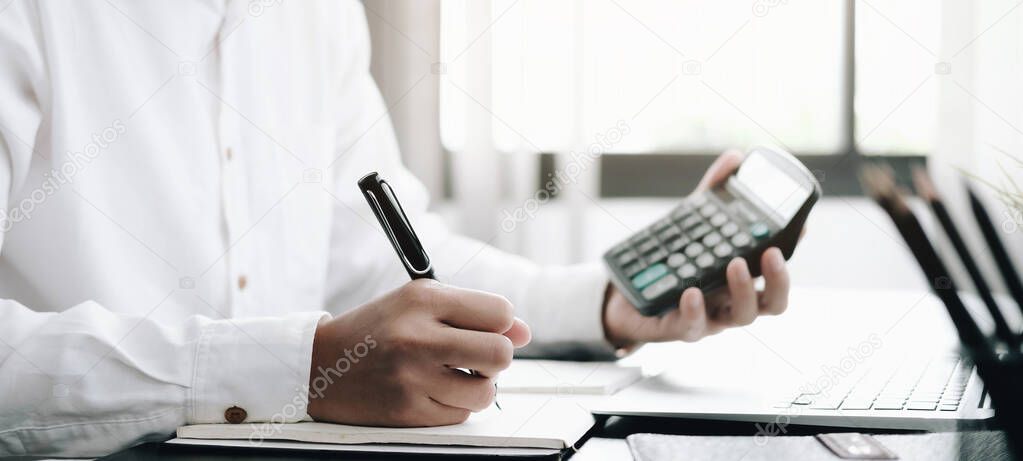 Close up Business man using calculator and laptop for do math finance on wooden desk in office and business working background, tax, accounting, statistics and analytic research concept