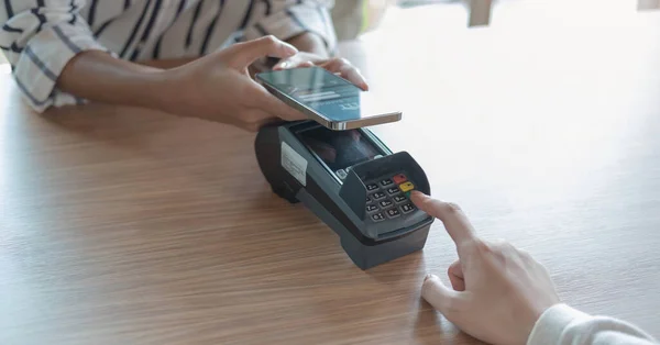 Woman paying bill through smartphone using NFC technology in a coffee. customer paying through mobile phone using contactless technology. Closeup hands of mobile payment at a coffee shop