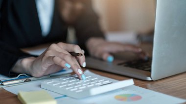 Hesap makinesi ve dizüstü bilgisayarı kullanarak ahşap masa, vergi, muhasebe, istatistik ve analitik araştırma konseptine matematik finansmanı sağlayan İş kadını kapat