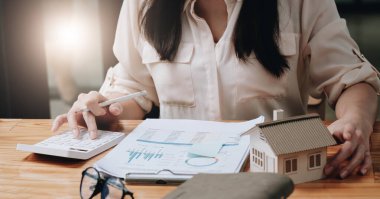 Ev modeliyle emlak satın almak için finansal tablo hazırlayan bir kadın. Para Kaydetme Kutusu