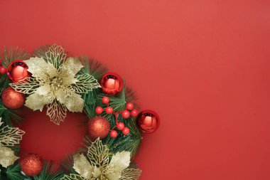 Çok güzel dekore edilmiş bir Noel çelengi. Canlı kırmızı arka planda altın aksanlı. Tatil dekorasyonu için mükemmel..