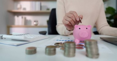 Bir insan, gelecek hedefleri için mali planlama ve tasarrufu sembolize ederek kumbaraya para yatırır..