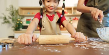 Genç bir kız annesiyle tatil süslemeleriyle dolu bir mutfakta yemek pişirirken hamuru neşeyle sarıyor..