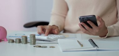 Bir kişi para ve mali belgelerle çevrili mali işler için bir hesap makinesi ve akıllı telefon kullanır. Bütçe ve mali planlama kavramı.