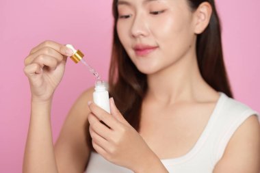 Genç bir kadın deri yüzme rutinini bir şişeden serum uygulayarak gösterir. Güzelliği ve kendine bakımı teşvik eder..