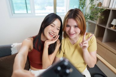 İki genç kadın mutlu bir anı paylaşıyor, selfie çekiyorlar ve samimi bir mekanda arkadaşlıklarını ifade ediyorlar..