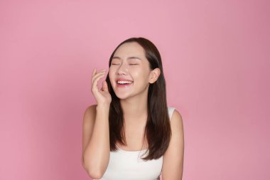 Cilt bakımı yaparken gülümseyen neşeli genç bir kadın mutluluk ve güven saçıyor. Pembe arka plan güzellik temasını güçlendirir.