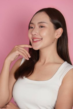 Kendine güvenen bir kadın gülümseyerek poz verir, güzelliğini ve cildini canlı bir ortamda gösterir..