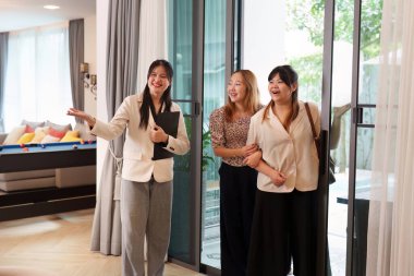 Bir emlakçı hevesle ilgi duyan müşterilere çarpıcı bir evin özelliklerine dikkat çekerek heyecanı teşvik eder..