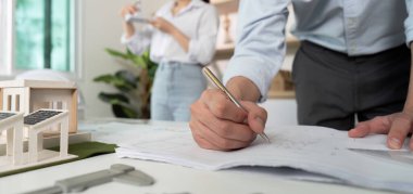 Bir adam bir kadının önünde bir kağıt parçasına yazı yazıyor. Adam mavi bir gömlek giyiyor ve kadın beyaz bir gömlek giyiyor.