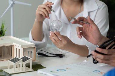 İki kişi bir proje üzerinde çalışıyor, birinin elinde ampul var. Sahne odaklı ve kararlı