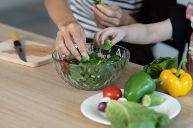 Bir kadın ve bir çocuk birlikte salata hazırlıyorlar. Salata marul, domates ve biber de dahil olmak üzere sebzelerle dolu. Kadın bir bıçakla sebzeleri kesiyor.