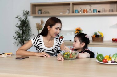 Bir kadın ve bir çocuk birlikte sebze yiyorlar. Kadın gülümsüyor ve çocuk salata yiyor.
