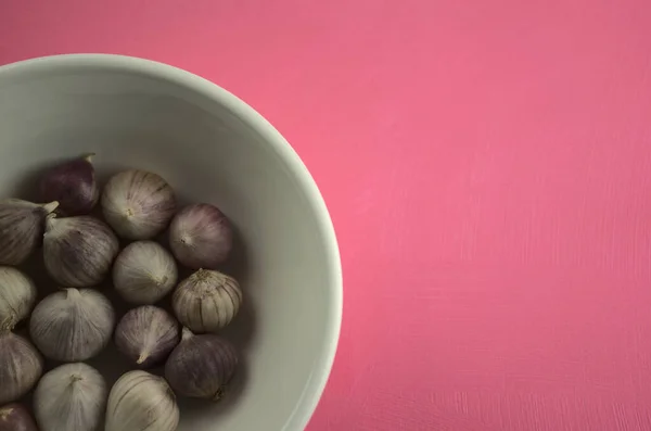 Garlic in bowl on acrylic scratchy pink canvas background. Food, kitchen, eating, still life photography with copy space.