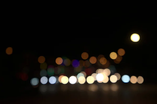 Blurry floating bokeh combination of cars on the road and street lights at the intersection, outdoor in modern big city. Beautiful blurred lights of dark night abstract. Horizontal, front view.