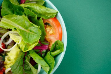Sebze salatası. Vejetaryen, vejetaryen, sağlıklı, yeşil kağıt arka planda yeşil kasede besleyici bir yemek. Marul, dilimlenmiş soğan, domates, romaine veya ana malzemelerde marul ve İsviçre pazarı..