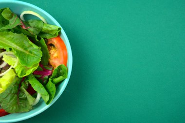 Sebze salatası. Vejetaryen, vejetaryen, sağlıklı, yeşil kağıt arka planda yeşil kasede besleyici bir yemek. Marul, dilimlenmiş soğan, domates, romaine veya ana malzemelerde marul ve İsviçre pazarı..