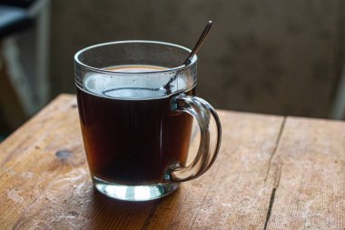 Kahveli cam bardak ve eski ahşap bir masada metal kaşık.