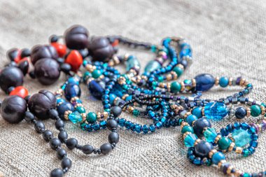 Değişik malzemelerden yapılmış boncuk ve kolyeler gri bir kumaş üzerinde bulunur. Küçük kızın hazineleri.