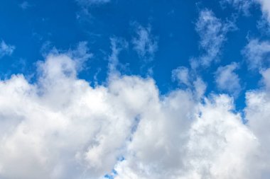 Güneşli bir bahar gününde beyaz bulutlar parlak mavi bir gökyüzünde süzülür.