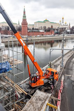Moskova, Rusya, 03.18.2021. Moskova Nehri 'nin üzerindeki Büyük Taş Köprüsü' nün yanında Kremlin Tepesi 'nin arka planında turuncu bir vinç var.