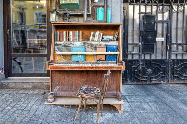 İçinde posta kutuları ve kitaplar olan eski bir piyano ve üstünde de eski resim çerçeveleri ve gaz lambaları. Yanında eski püskü bir Viyana sandalyesi var.