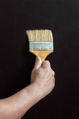 Büyük, karanlık bir yüzeyin arka planında fırçalı bir işçinin erkek eli.