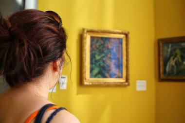 Sarı duvarlar ve sanat müzesinde tabloları olan kahverengi saçlı bir kadın.