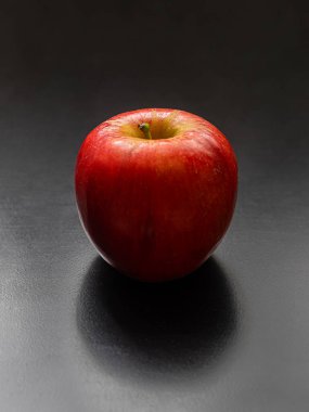 Mutfak masasının koyu arka planında parlak derili olgun kırmızı bir elma.
