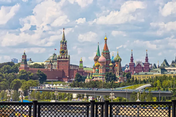Moskova, Rusya, 06.15.2021. Yüzen köprüsü olan Zaryadye Parkı, Kremlin kuleleri ve St. Bulutlu gökyüzüne karşı Basil Katedrali