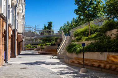 Güneşli bir günde serin gölgeli bankları, merdivenleri, yeşil ağaçları olan bir dinlenme alanı.