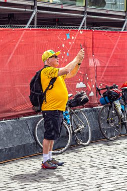 Moskova, Rusya, 06.14.2018. Sırt çantalı, sarı tişörtlü ve beysbol şapkalı yaşlı bir turist akıllı telefonuyla etrafındaki manzaranın fotoğrafını çekiyor.