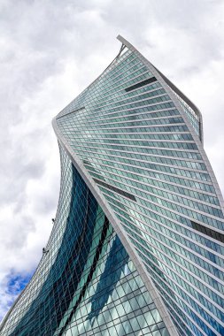 Moskova, Rusya, 08.07.2021. Moskova 'nın iş merkezindeki Evrim Kulesi. Gökdelen bulutlu gökyüzüne doğru döner. Duvarda sanayi tırmanışçılarının küçük figürleri asılı.