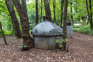 Şehir parkındaki ağaçlar arasındaki yeşil yaprakların arka planında eski kapalı bir kanalizasyon.