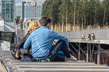 Bir adam ve bir kız güneşli bir günde köprünün geniş korkuluğunda oturuyorlar.