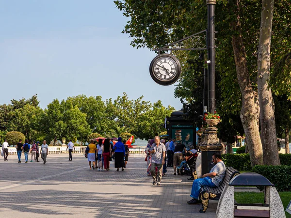 Bakü, Azerbaycan, 07.26.2019. Bakü 'nün Primorsky Bulvarı' nda gezip dinlenen insanlar. Eğlence bankları, saatli bir sokak lambası.