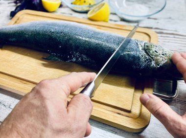 Açık tenli bir adam pişirmek için çiğ balık keser..