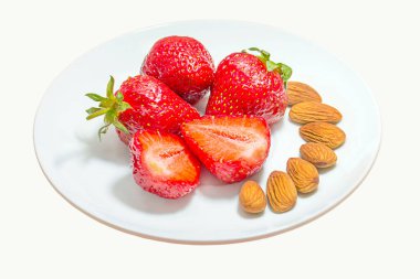 Beyaz arka planda beyaz bir tabakta taze çilek ve badem.