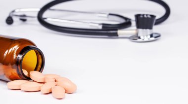 Sarı haplı kahverengi cam şişe ve beyaz arka planda steteskop.