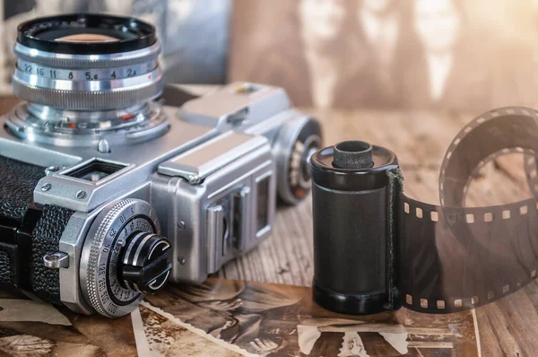 still life with retro analog camera, camera roll and old photos on wood background