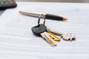 Dostça bir bölgede yeni bir ev alma heyecanı sırasında ev anahtarlarını önemli evrak işlerinin üstünde tutan eller..