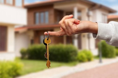 Yeni ev sahipliğinin heyecanını sembolize eden, hareketli bir mahalle ortamındaki anahtarları tutan eller..