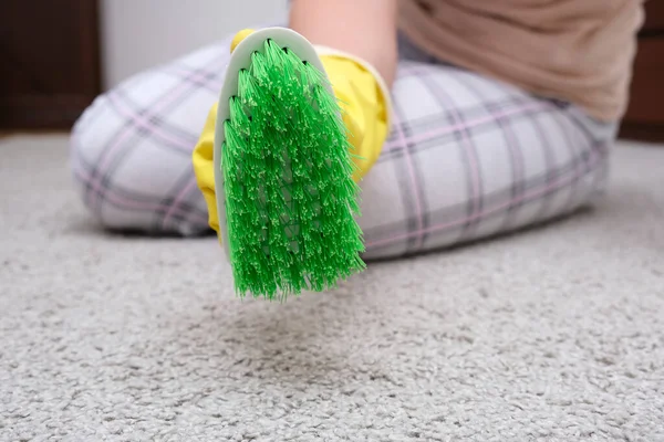 Vrouw in gele handschoenen met een groene borstel reinigen en poetsen tapijt, het verwijderen van vlekken en wol uit het en het doen van routine huiswerk — Stockfoto
