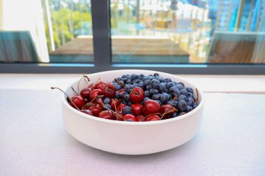 Beyaz seramik bir tabakta taze kiraz ve yaban mersini dolu çiğ meyve..