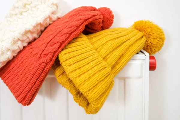 Colorful winter knitted caps, hats hanging and drying on a hot central heating radiator, winter family outdoor activities and sports concept — Stock Photo, Image