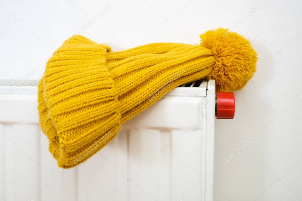 Colorful yellow winter knitted cap, hat hanging and drying on a hot central heating radiator, winter outdoor sport activities concept